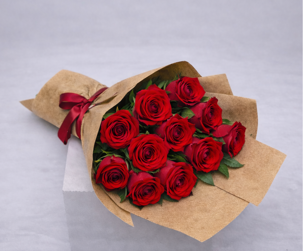 Bouquet of red roses wrapped in brown paper with a red ribbon on a light gray background