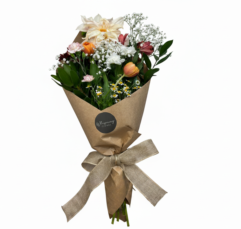 A floral bouquet wrapped in brown kraft paper and tied with a beige ribbon, displayed in a clear glass vase on a wooden surface against a white background.