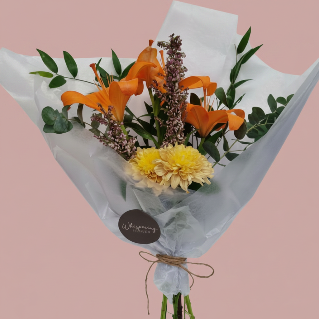 A floral bouquet wrapped in white tissue paper, featuring orange lilies, yellow chrysanthemums, green foliage, and small purple filler flowers, tied with twine and a round 'Whispering Flowers' label.