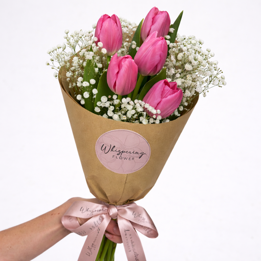 Bouquet of pink tulips wrapped in brown paper with a pink ribbon and 'Whispering Flower' label.
