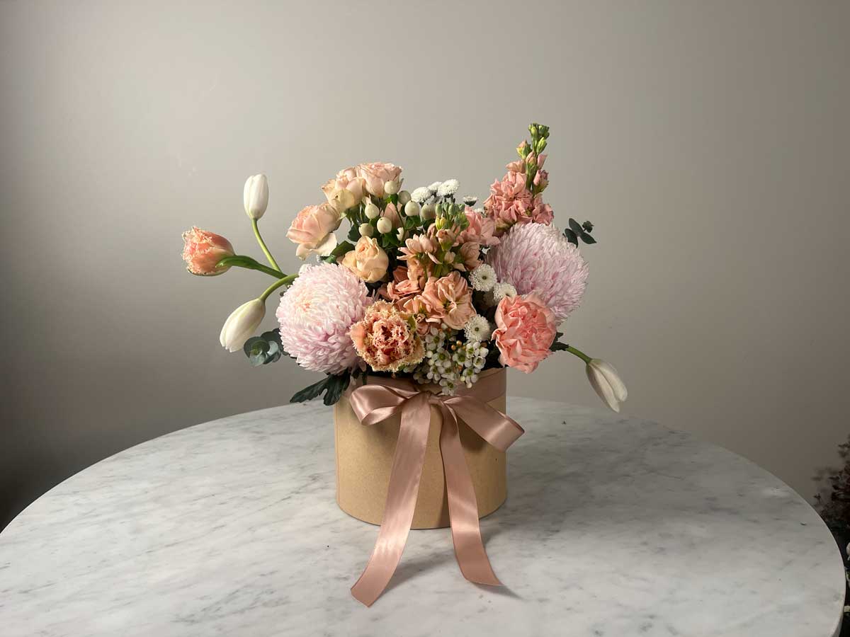 Floral arrangement in a box with a pink ribbon on a marble surface.