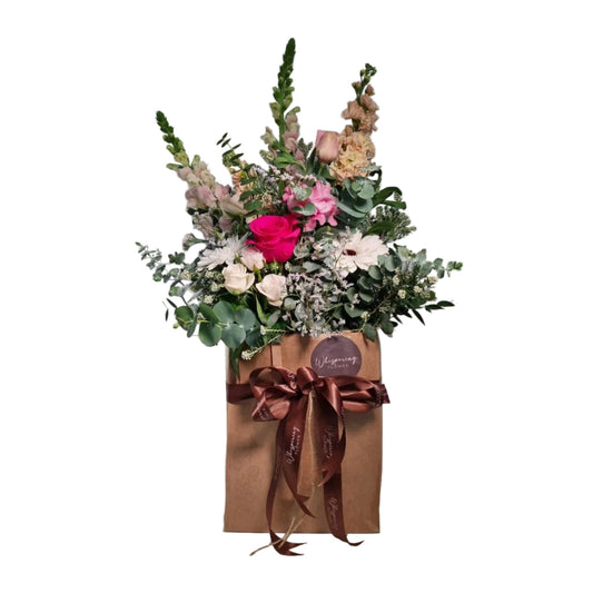 Pink, white and peach bouquet in a brown paper gift bag tied with a brown ribbon and wax seal