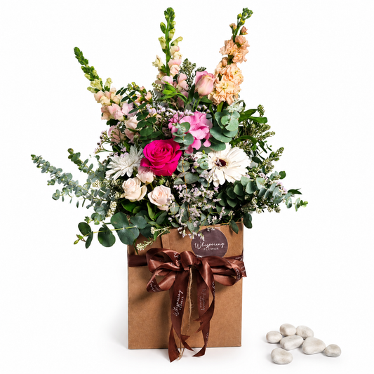 Close-up of a bright bouquet with roses, gerbera and snapdragons in a kraft paper gift bag.