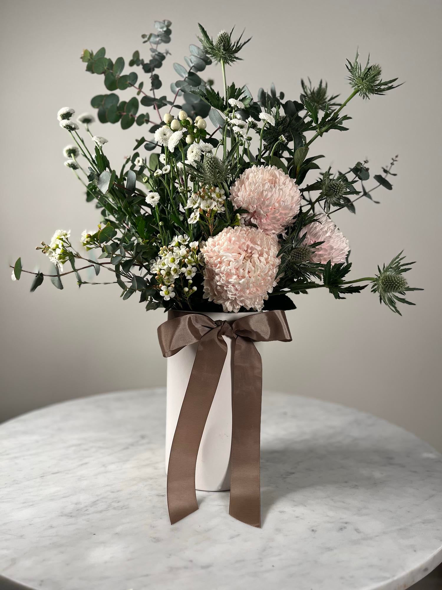 Bouquet of flowers with a brown ribbon in a white vase on a marble surface.