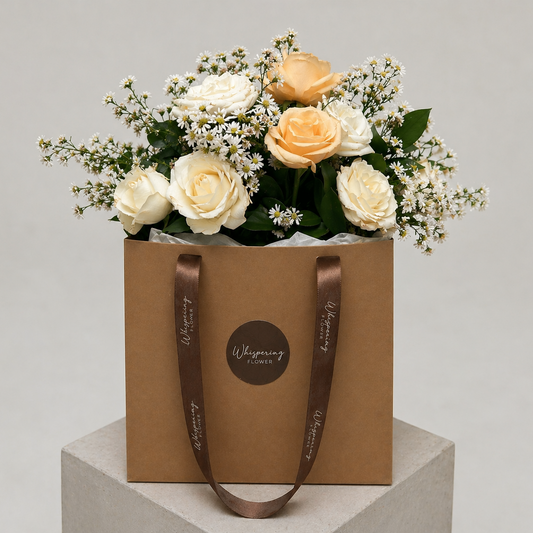 Golden Bloom Mother's Day bouquet — cream and butter roses, white lisianthus, and gypsophila arranged in a kraft hatbox with brown satin handles. Auckland florist delivery.