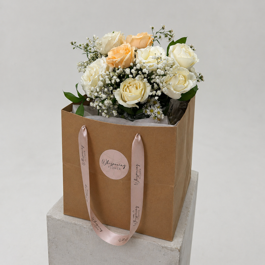 Golden Bloom Mother's Day bouquet — cream and butter roses, white lisianthus, and gypsophila arranged in a kraft hatbox with brown satin handles. Auckland florist delivery.