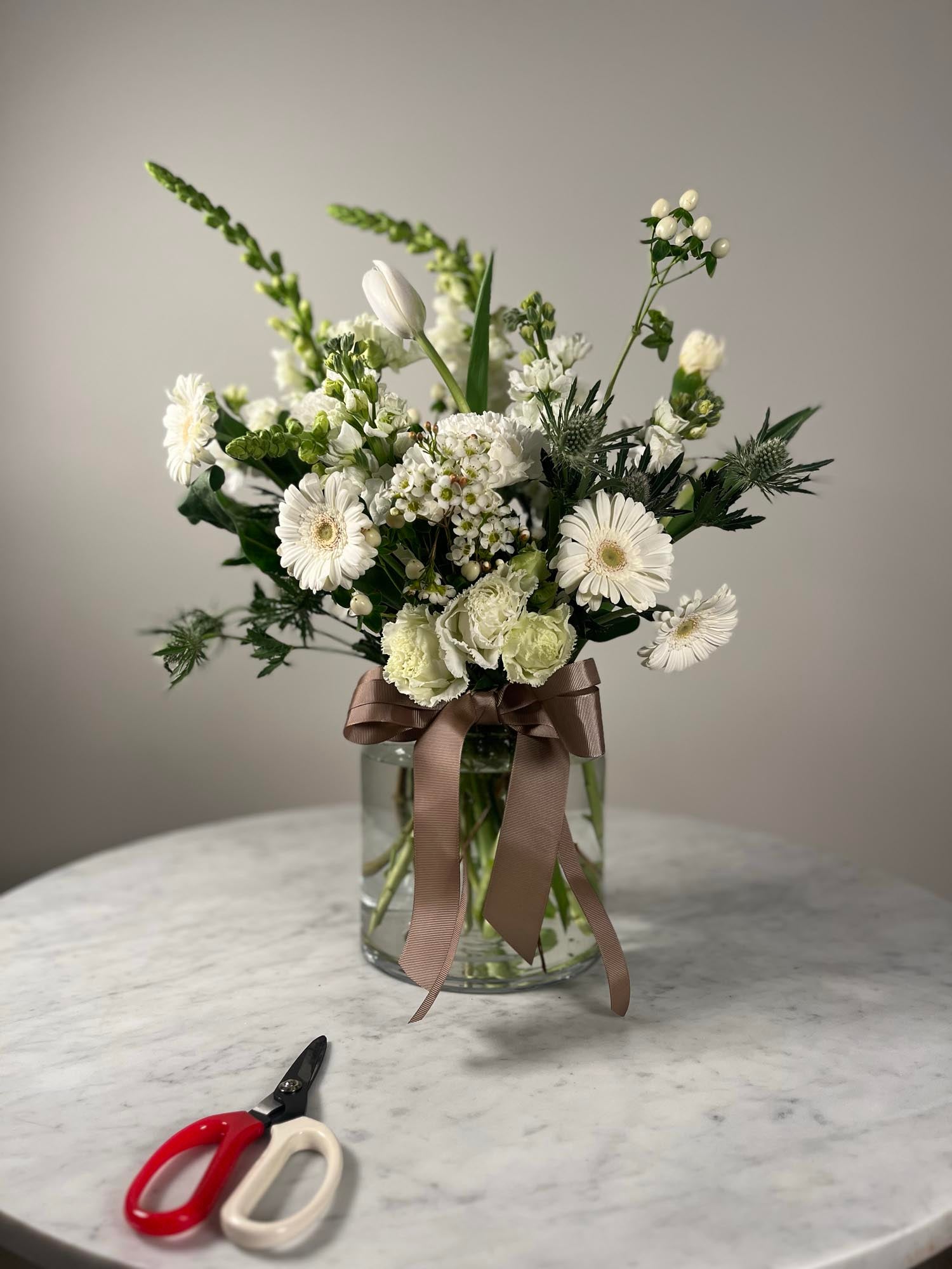 Bouquet of white flowers in a clear vase on a marble surface with scissors.