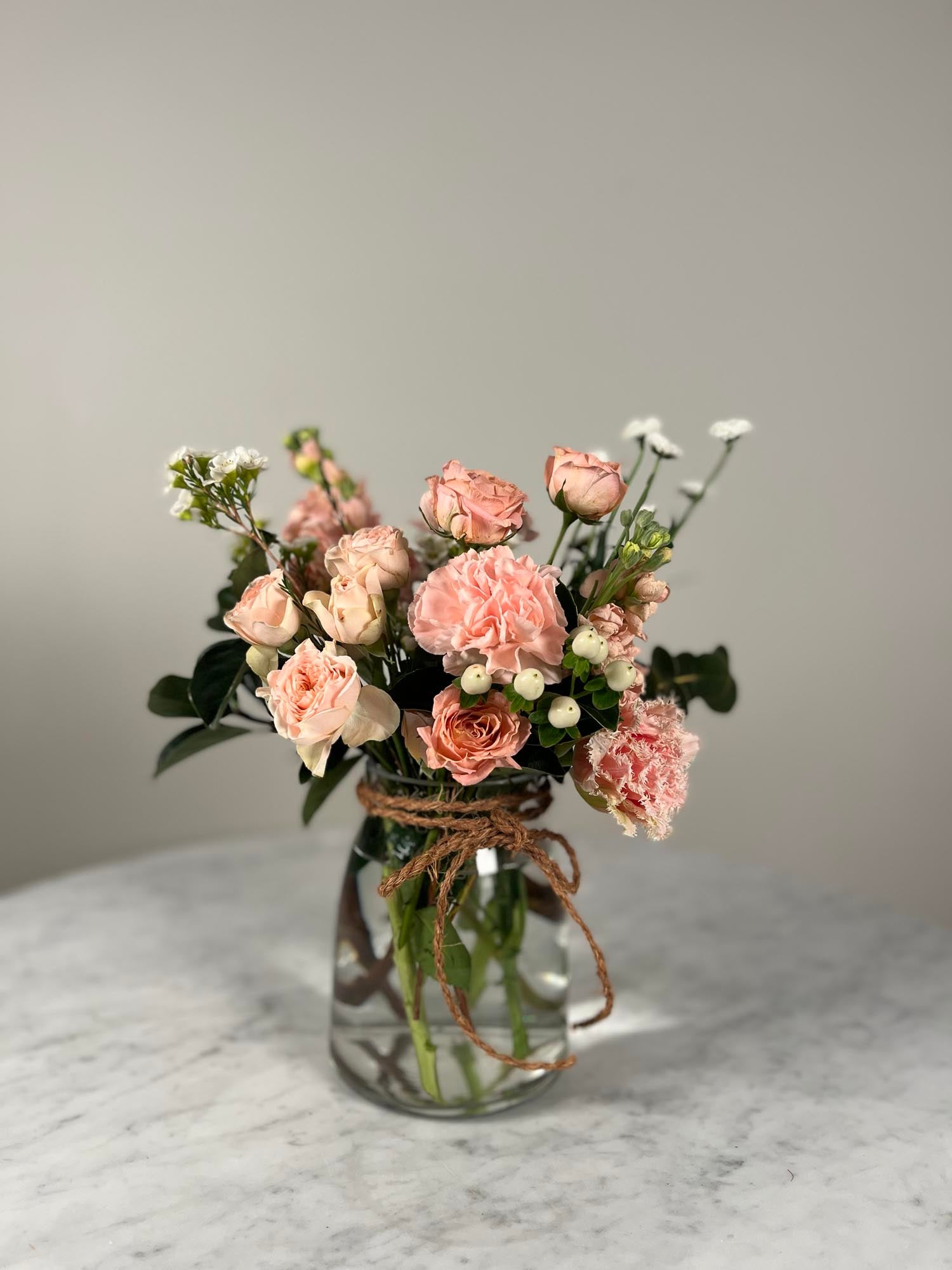 Bouquet of pink and white flowers in a clear glass vase on a marble surface with a neutral background