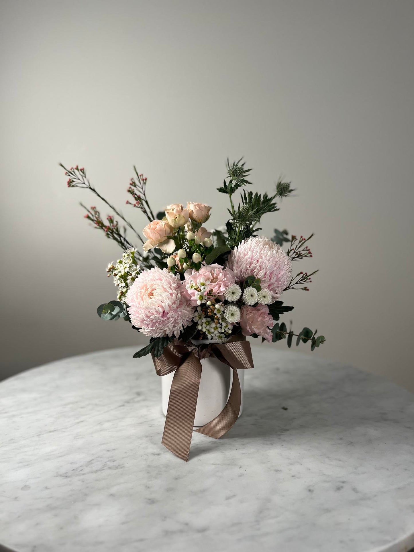 Bouquet of pink flowers in a white vase on a marble surface with a neutral background