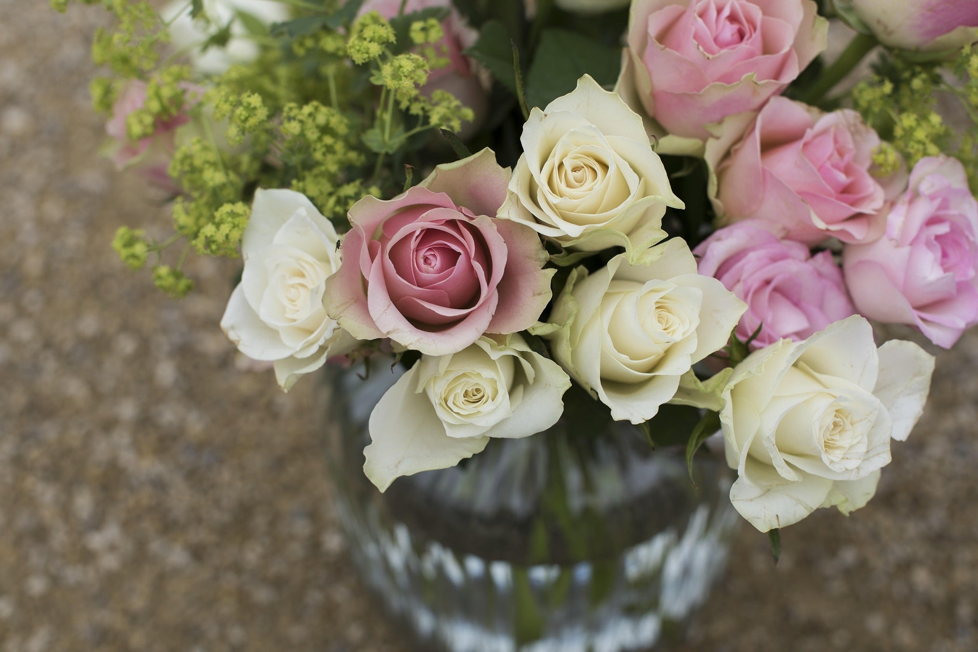 Bouquet of pink and white roses in a clear vase on a textured surface