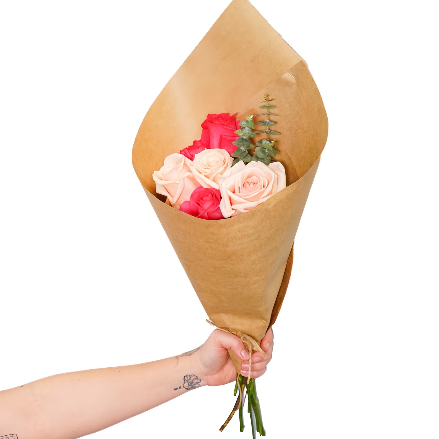A hand holding a small bouquet of pink and red roses wrapped in brown kraft paper, isolated on a white background.